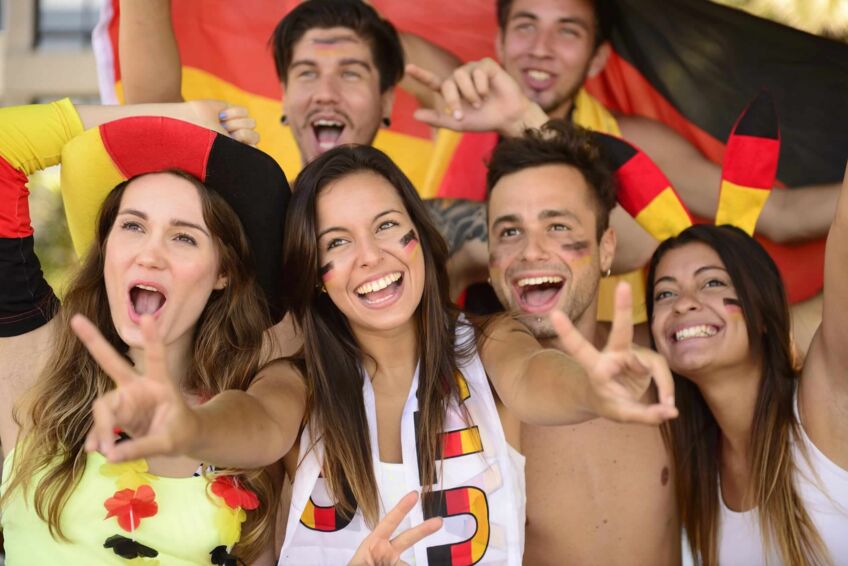 Eine Gruppe von Deutschlandsfans (Frauen und Männer) schauen begeistert einem Fußballspiel zu.